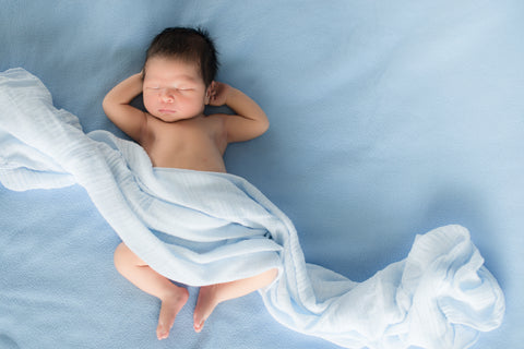 em bé nằm ngủ trên giường màu xanh dương, một tấm lụa xanh dương chạy ngang người