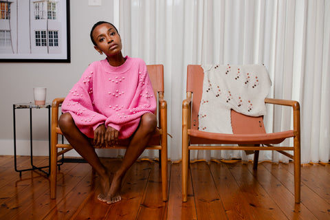 Sinead sitting on a stylish chair wearing the Cosmic Pink bobble knit sweater.
