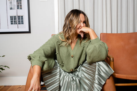 Amie Rohan sitting in the lounge wearing the bowie bobble knit cardigan in sage with a soft sage pleated midi skirt