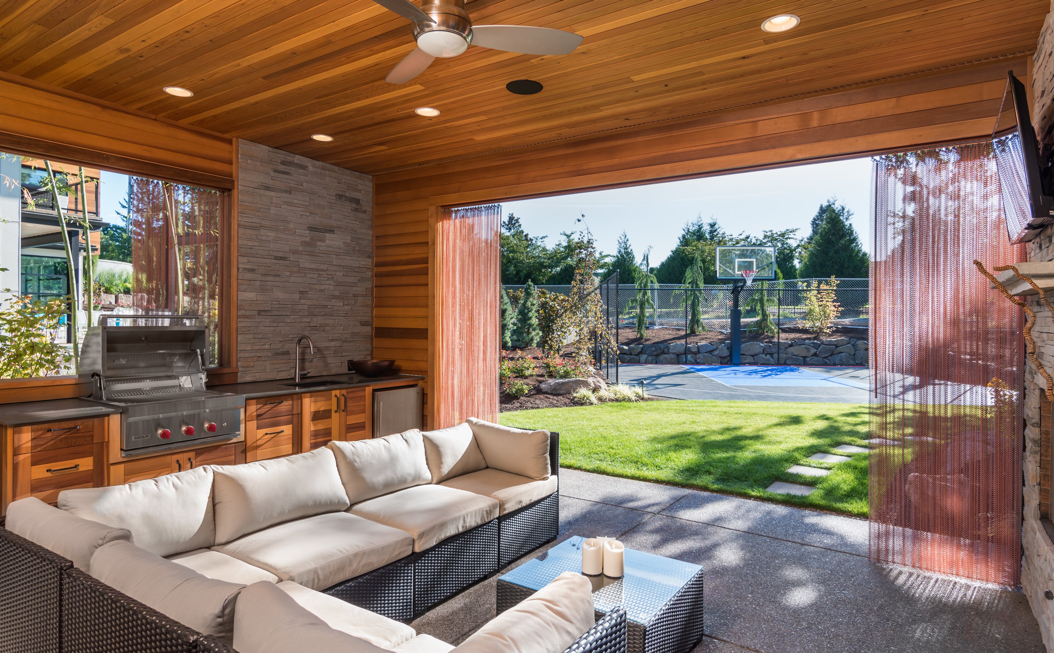 Covered outdoor porch with an outdoor kitchen, and lounge seating overlooking a backyard with a half basketball court.