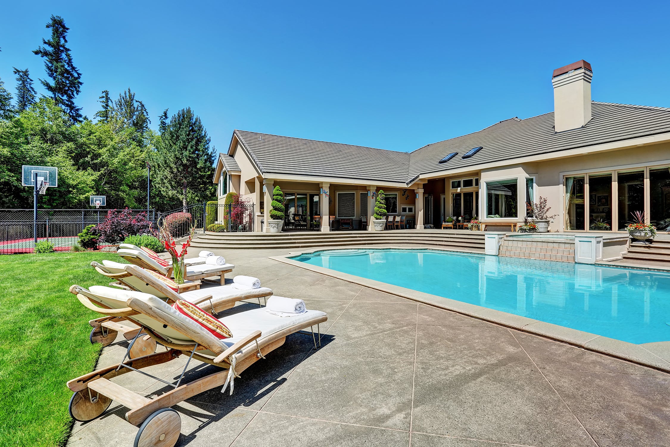 Backyard pool with loungers on the side. The house is in the background and it is a bright spring or summer day.