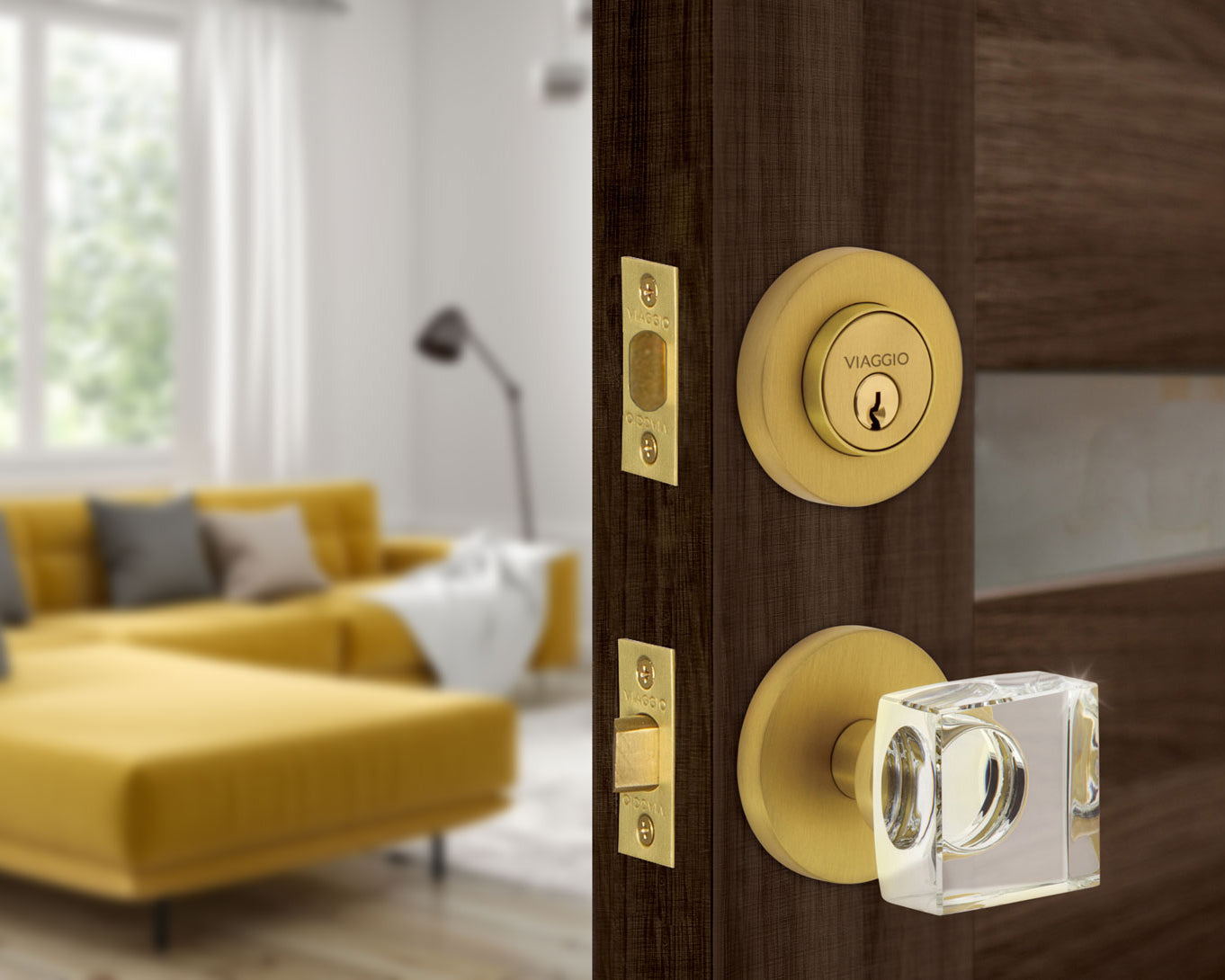 Circolo Rosette Entry Set with Quadrato Crystal Knob in Satin Brass on an entry door walking into a living room with a yellow sofa.