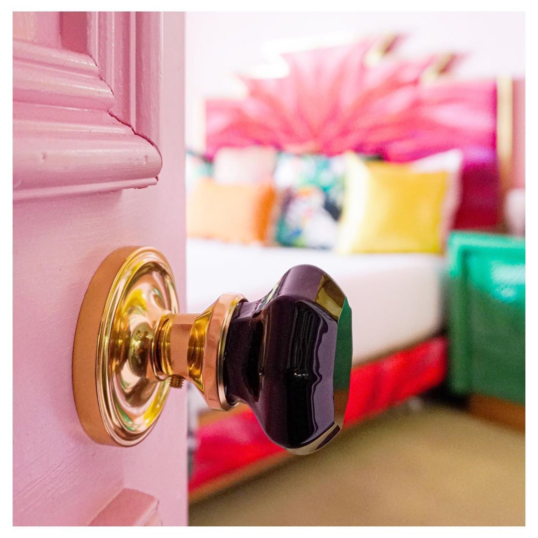 A pink door leading into a vibrant room with a Nostalgic Warehouse Classic Rosette with Black Waldorf Knob in Unlacquered Brass door knob on it.