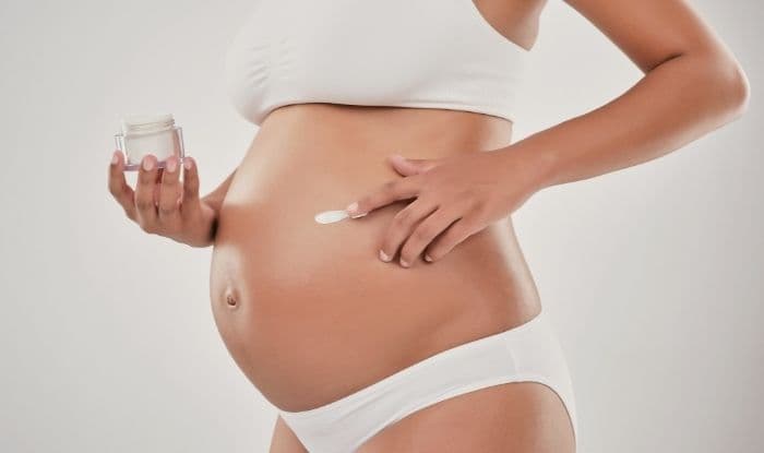 A pregnant woman applies moisturizer to her belly to prevent pregnancy strech marks.