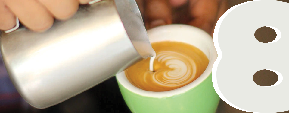 A Honolulu Coffee barista pouring latte art into a cappuccino cup.