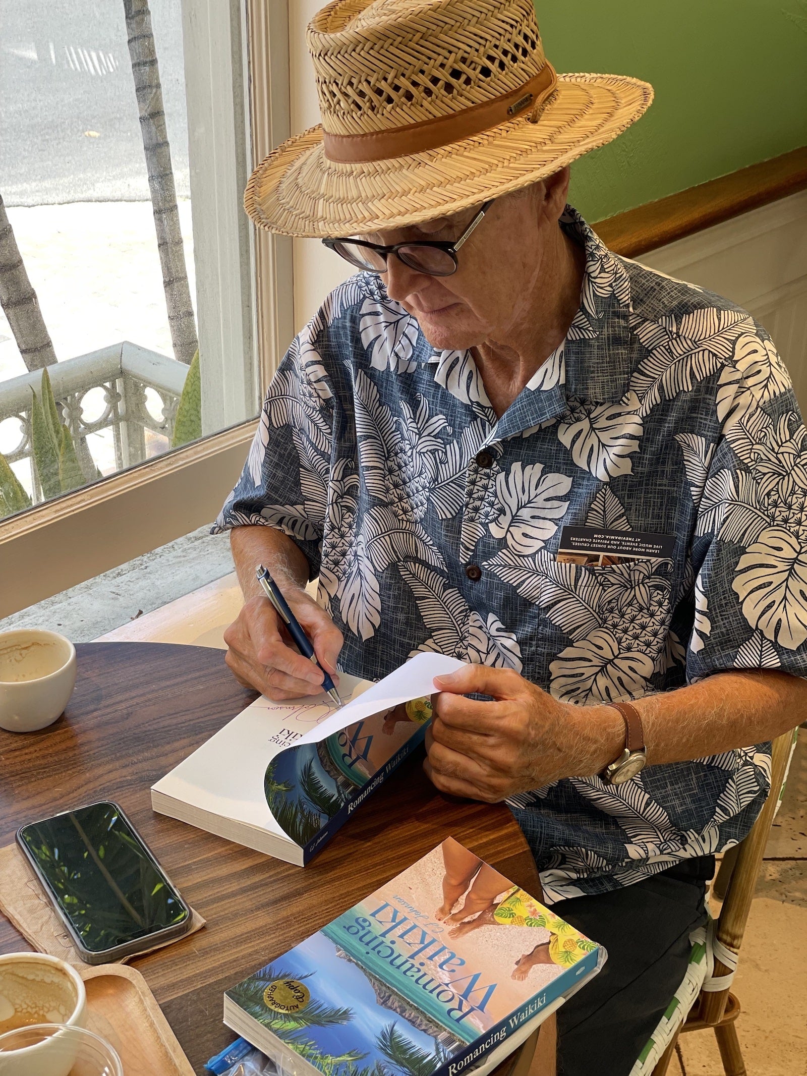 Charles signing a book inside the Honolulu Coffee Moana Surfrider cafe