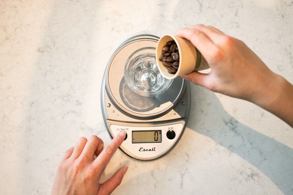 Pouring coffee beans into a cup to weight out 24 grams of coffee beans using a scale.