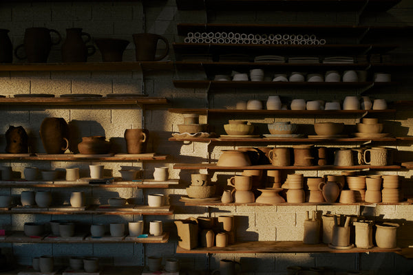 Pottery members work sitting on shelves.