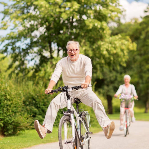 una pareja de ancianos andando en bicicleta junto con árboles verdes en el fondo