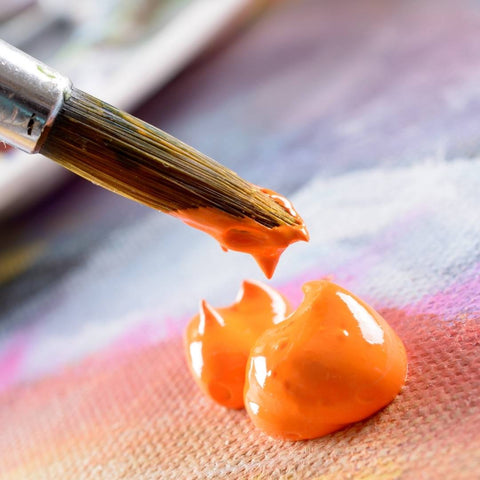 Un pincel sumergido en pintura de color naranja.