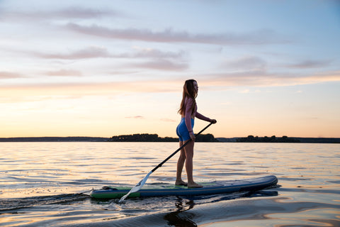 beautiful woman paddle boarding on a clam lake, with sunset