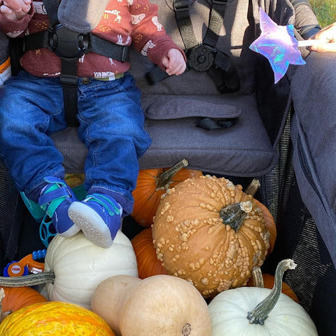 A toddler lounging around in a stroller wagon full of pumpkins