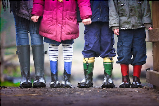 Four kids wearing dirty rain boots and warm and cozy autumn outfits