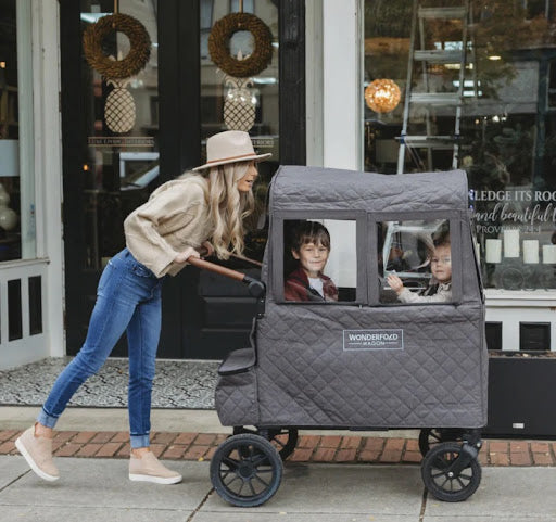 A smartly dressed mom pushing her kids in an enclosed stroller wagon