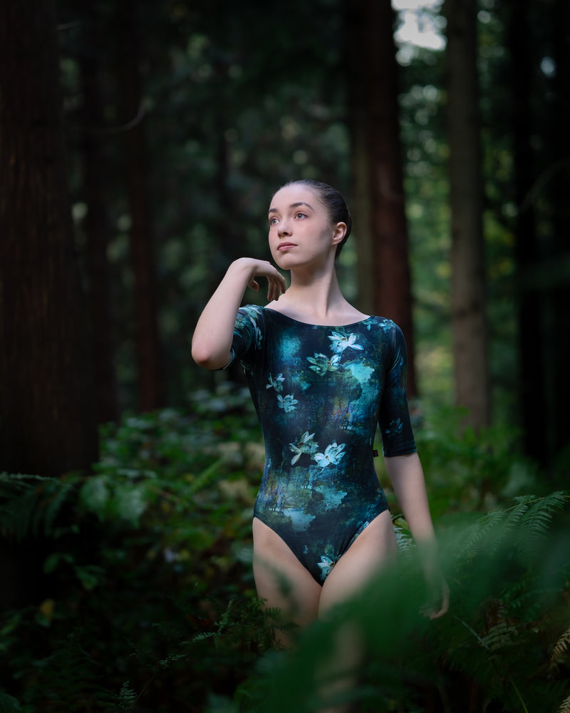 Dancer wearing a green forest print leotard with sleeves in woodland setting. 