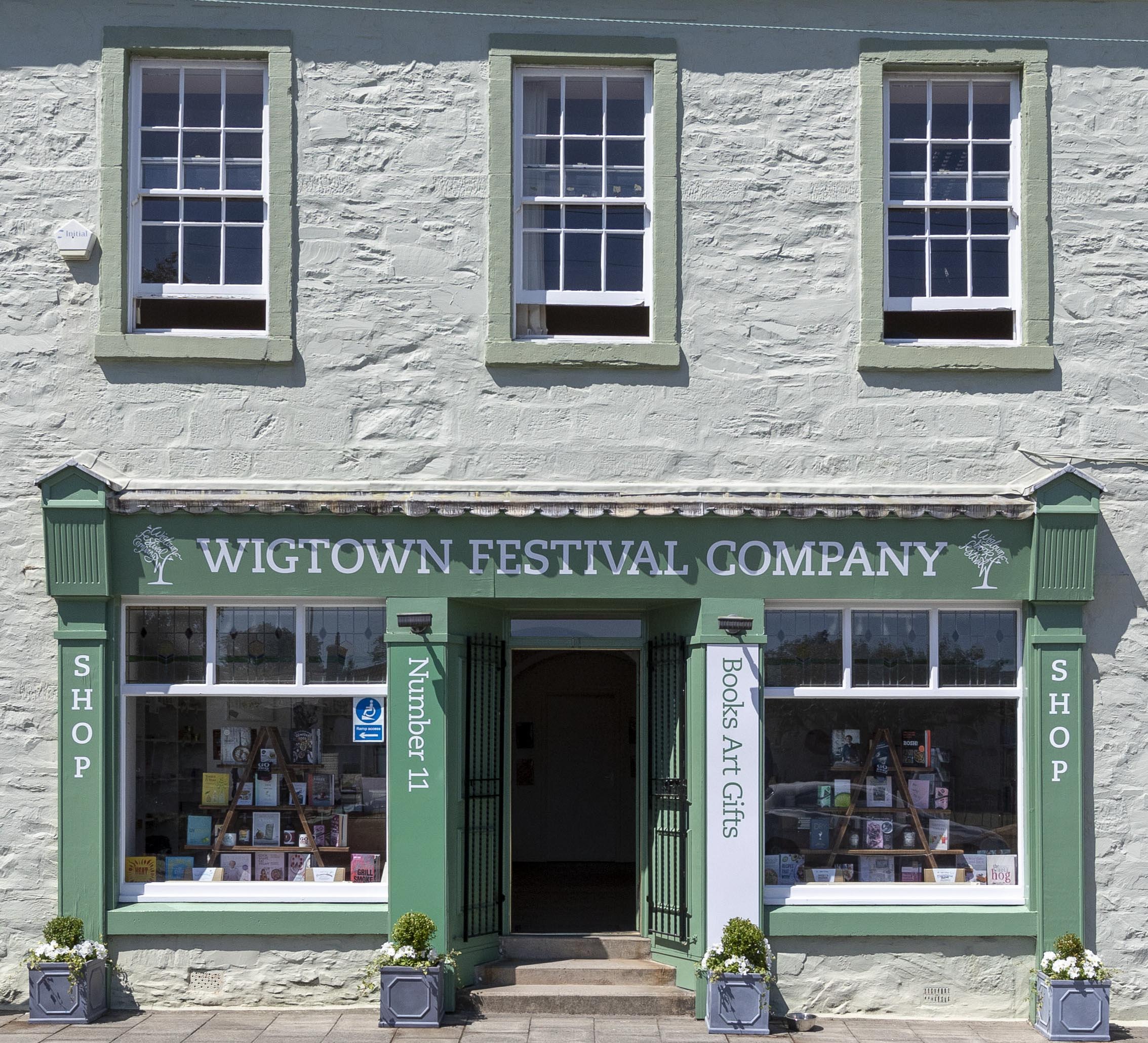 Exterior of the Wigtown Festival Company offices and bookshop, a historic building with facade painted green, two windows showing book displays.