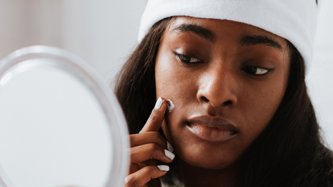 Woman with dry melanin rich skin looking in mirror