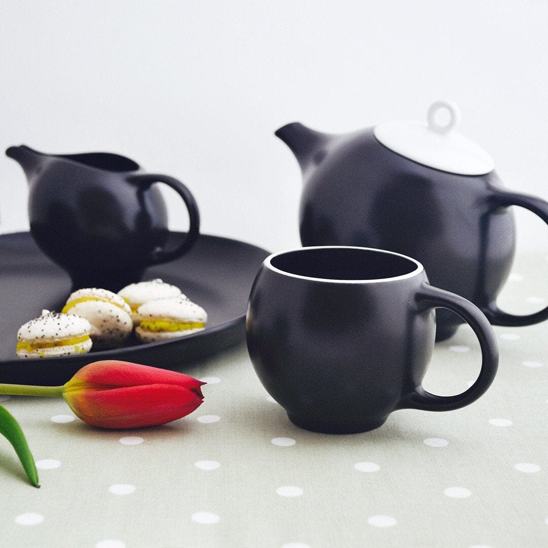 A black tea set on a table with a red tulip