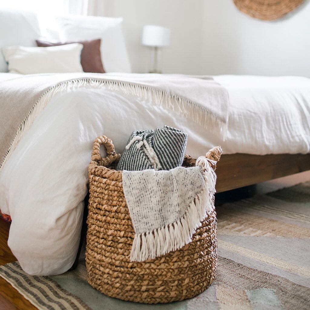 Woven basket holding throw blankets at the foot of the bed