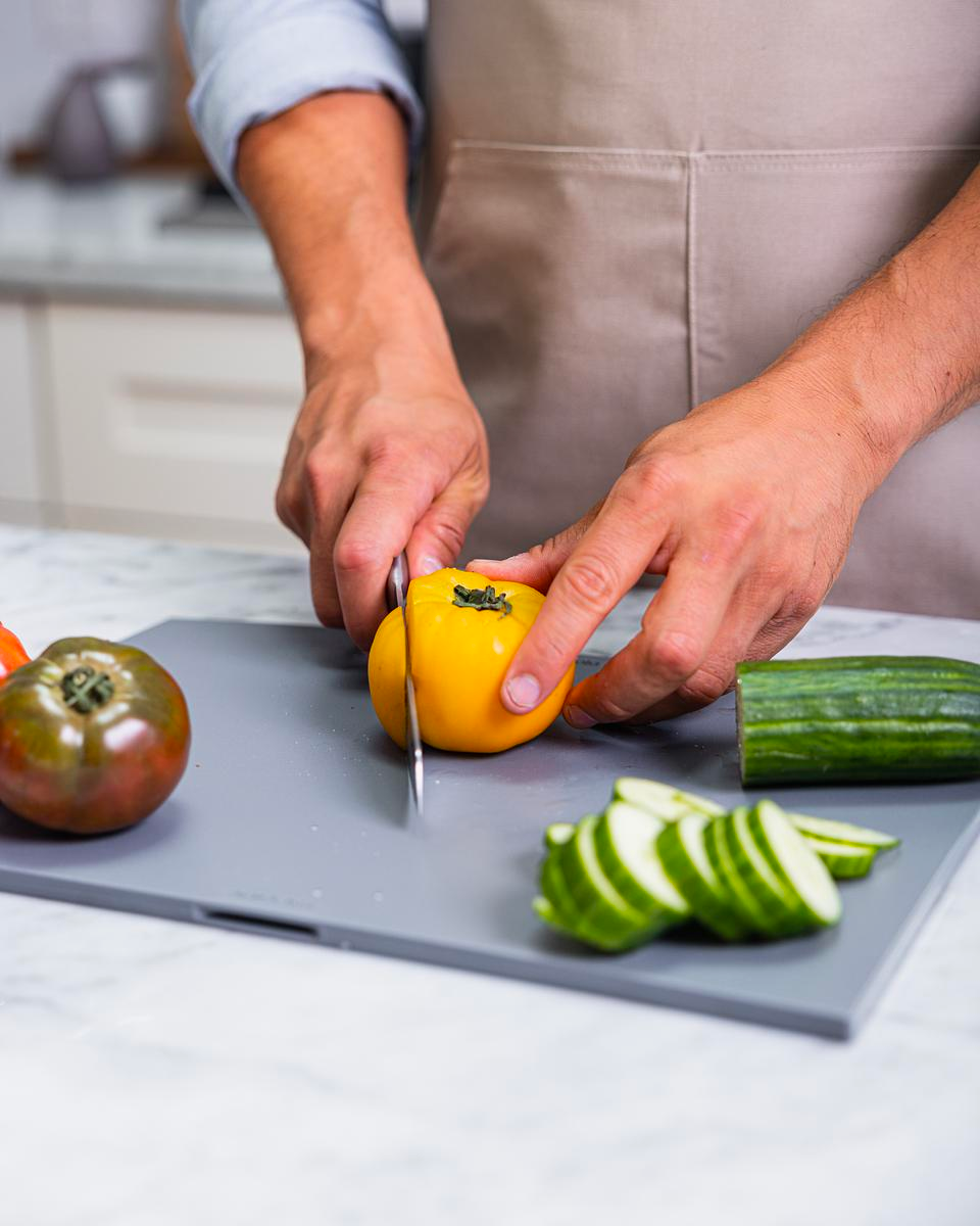 Man cuts a yellow tomato on a grey cutting board