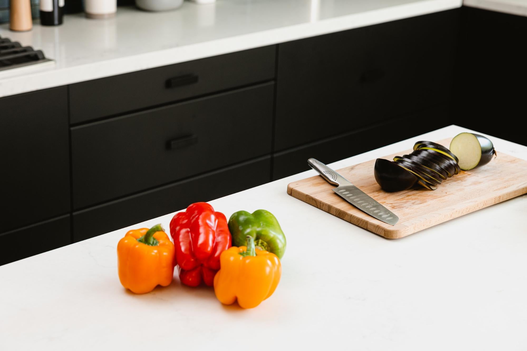 Bell peppers on the counter next to a cutting board with a knife and sliced eggplant.