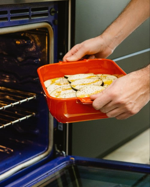Person placing red ceramic dish in oven