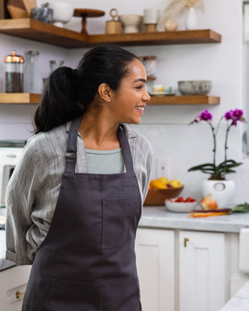 woman stands in kitchen with dark grey apron