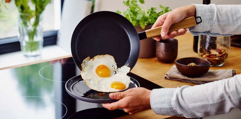 A person serving sunny side up omelet from fry pan to a plate