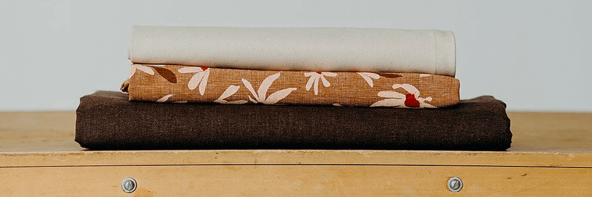 Three brown and cream natural linen tablecloths folded on top of a wooden bench