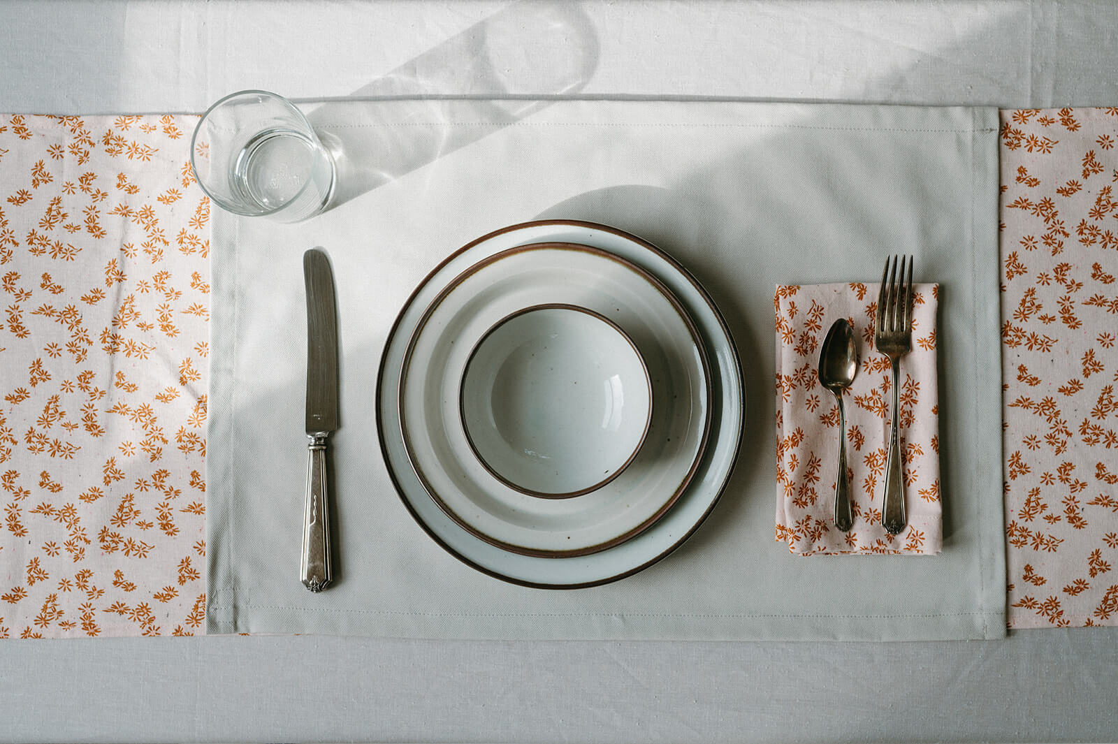 White plates and bowls on a white placemat with an orange floral napkin and table runner