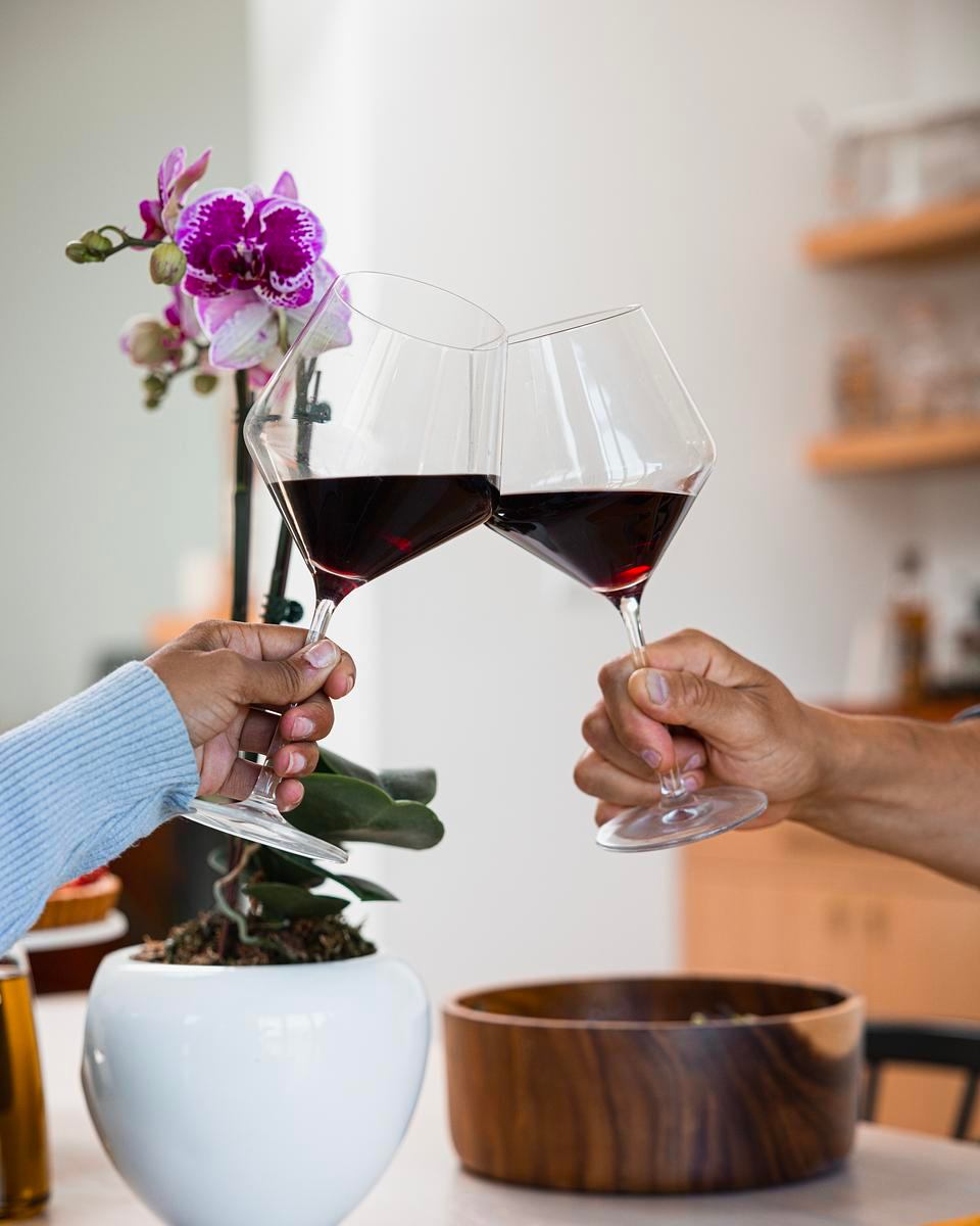 Two hands holding wine glasses over a table