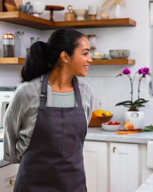 woman stands in kitchen with arms behind her wearing apron