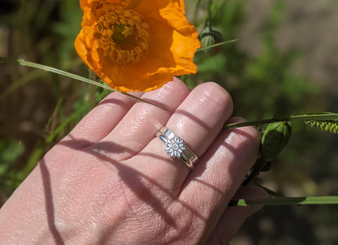 Two silver stacking rings, one with a flower detail and one plain, featuring garden scenery