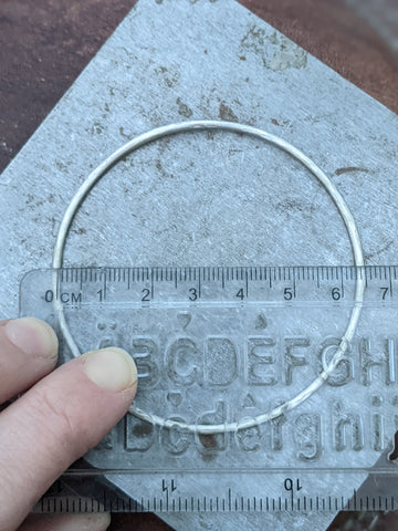 silver bangle with a ruler measuring the inside diameter. 