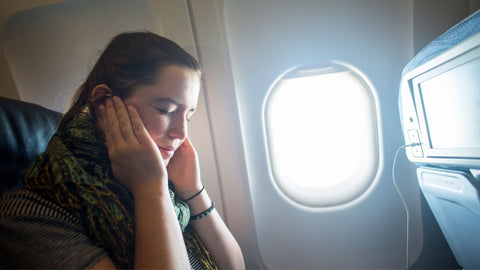 woman on a plane holding her ears in discomfort