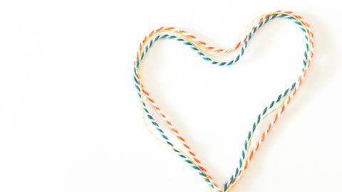 Turquoise, yellow, and orange striped cotton baker's twine is shown in a heart shape on a white background