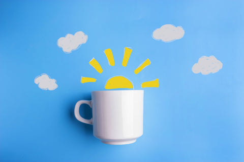 Coffee Cup With Drawn Sun Coming Out Of The Top on Blue Background With Clouds