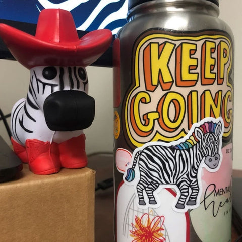 A metal water bottle is decorated with lots of stickers, including a zippy zebra sticker by Sunny Day Designs. Also shown is a zebra figurine wearing a red cowboy hat