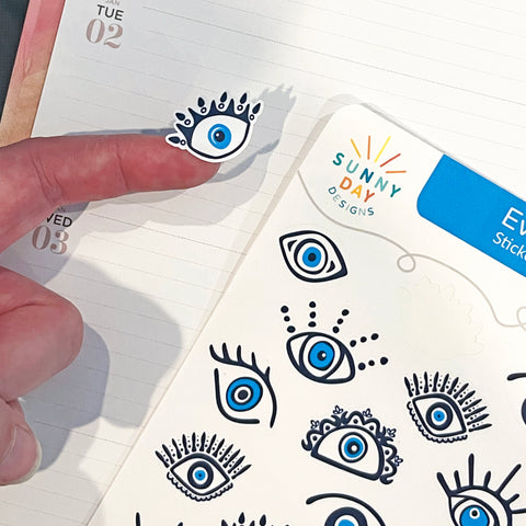 hand adding evil eye shaped stickers to a paper daily planner calendar