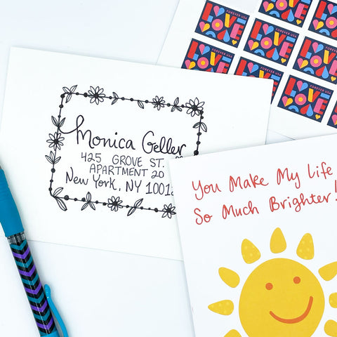 Pen pal letter-writing supplies: a sun greeting card, handwritten envelope with address and LOVE postage stamps on a white background