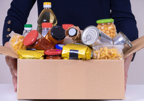 Person holding a cardboard box filled with groceries and food for a food pantry donation