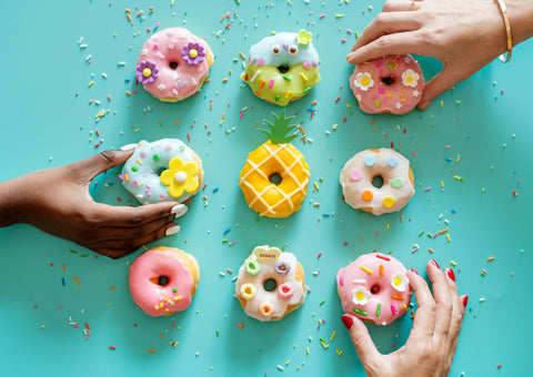 Hands of different skin tones reaching to grab colorful donuts from a turquoise background