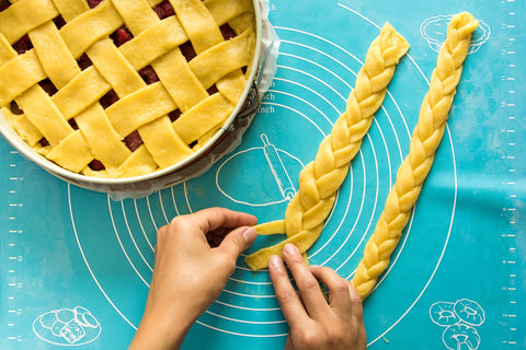 Hands braiding piecrust while making a homemade pie on a turquoise pastry mat