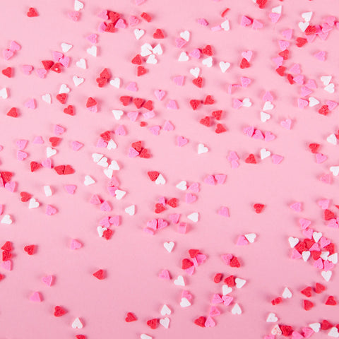 Red, pink and white heart-shaped spinkles scattered across a light pink background