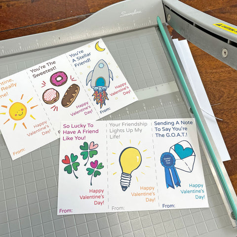 6 Printable DIY valentine cards by Sunny Day Designs being cut out using a gray paper cutter
