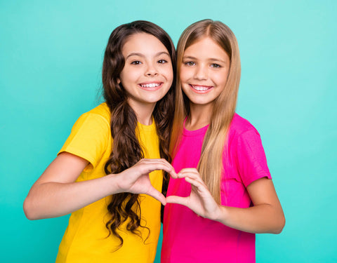 Two girls wearing yellow and pink shirts and holding their hands together to create a heart shape