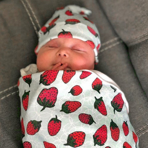 Bubbly Berries strawberry organic cotton baby blanket and hat by Sunny Day Designs. Image shows an adorable newborn baby wearing the strawberry hat and berry blanket. Made in the USA