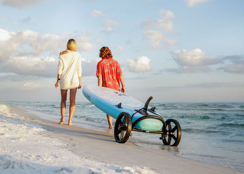 Paddle board wheels carried on the beach by couple