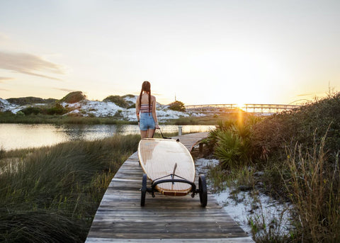 Paddle board wheels carried on the wooden broadwalk by girl