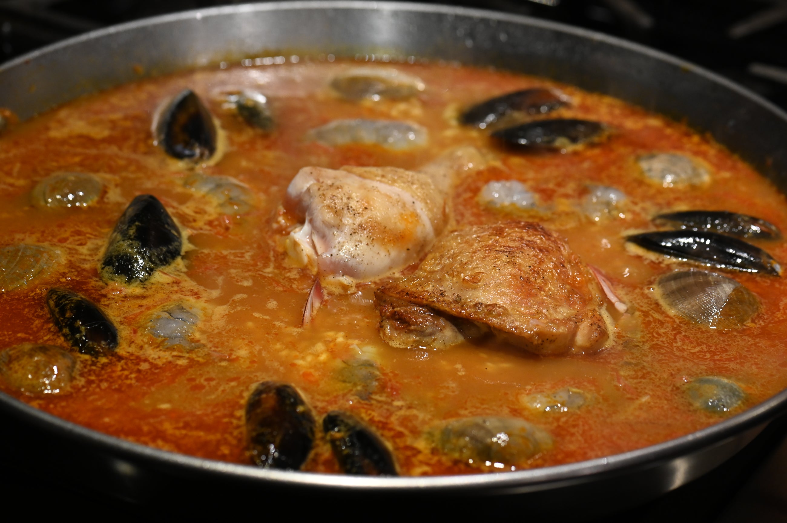 adding clams mussels shrimp to the paella pan